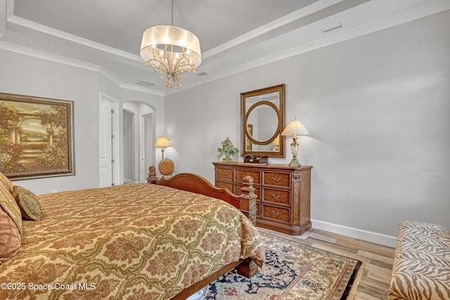 bedroom with visible vents, a tray ceiling, wood finished floors, arched walkways, and baseboards