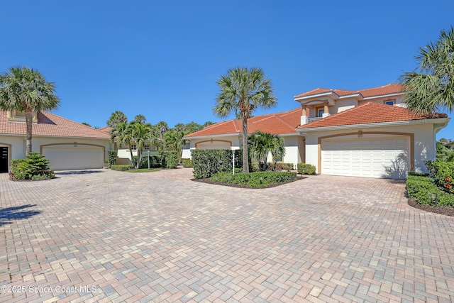 mediterranean / spanish-style house featuring a tile roof, decorative driveway, a garage, and stucco siding