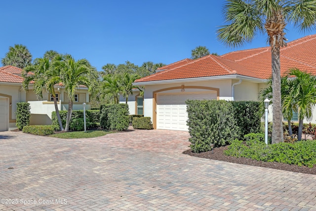 mediterranean / spanish home with stucco siding, a tiled roof, an attached garage, and decorative driveway