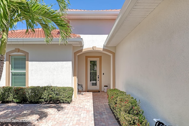 view of exterior entry with stucco siding and a tiled roof