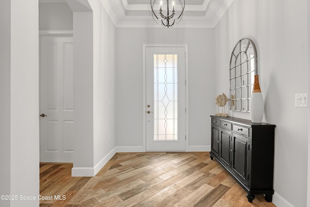 foyer with baseboards, light wood-style flooring, crown molding, a notable chandelier, and a raised ceiling