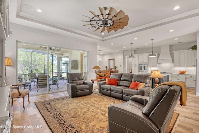 living room featuring a raised ceiling, light wood-type flooring, and ceiling fan