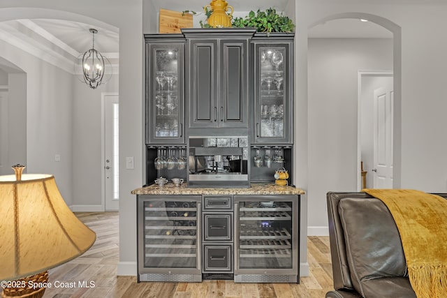 bar featuring light wood finished floors, crown molding, wine cooler, arched walkways, and a bar