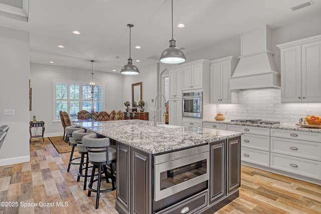 kitchen featuring visible vents, a kitchen bar, custom range hood, appliances with stainless steel finishes, and a sink