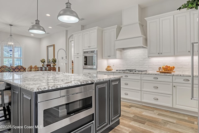 kitchen with white cabinets, stainless steel appliances, light wood-type flooring, and premium range hood