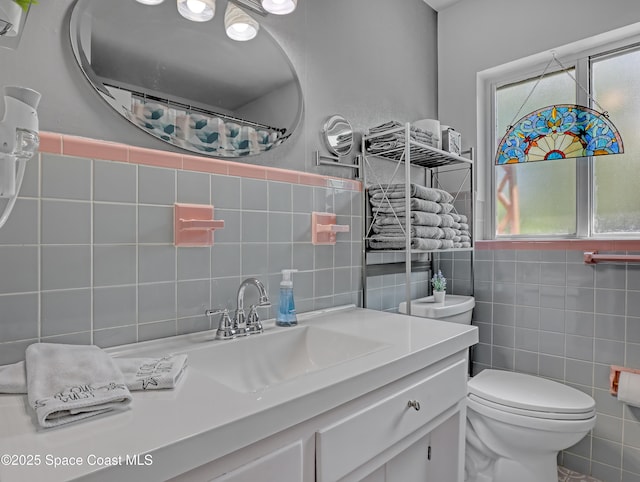 bathroom with a healthy amount of sunlight, tile walls, toilet, and vanity