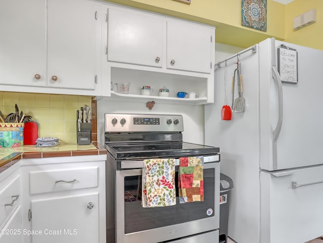 kitchen featuring stainless steel electric range oven, tile countertops, tasteful backsplash, freestanding refrigerator, and white cabinets