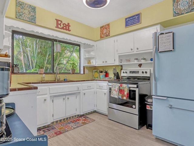 kitchen with white cabinets, tile countertops, freestanding refrigerator, stainless steel range with electric cooktop, and open shelves