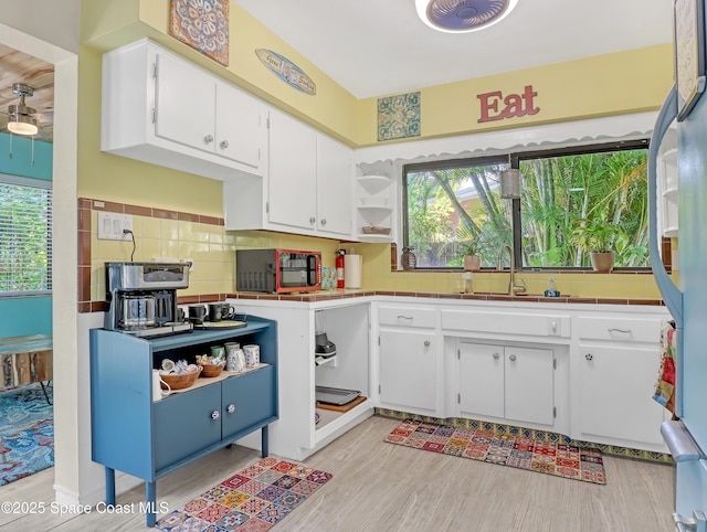 kitchen featuring tile countertops, a sink, white cabinets, backsplash, and open shelves