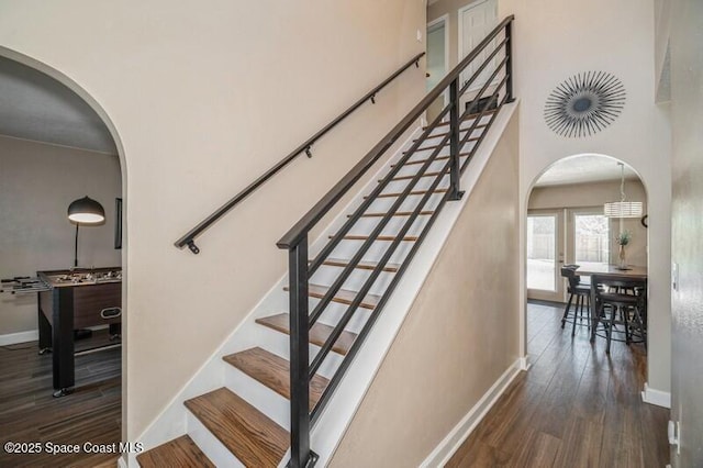 stairs with arched walkways, baseboards, and wood finished floors