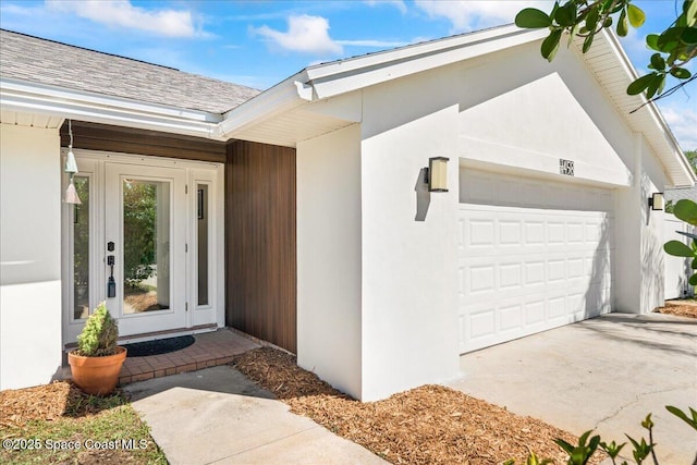 entrance to property featuring a garage, driveway, and stucco siding