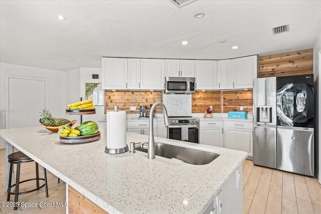 kitchen with visible vents, a kitchen island with sink, stainless steel appliances, white cabinetry, and a sink