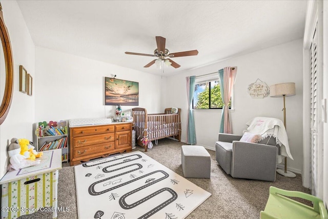 bedroom with a ceiling fan, carpet, a crib, and baseboards