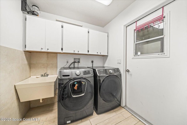 clothes washing area with cabinet space, a sink, tile walls, and separate washer and dryer