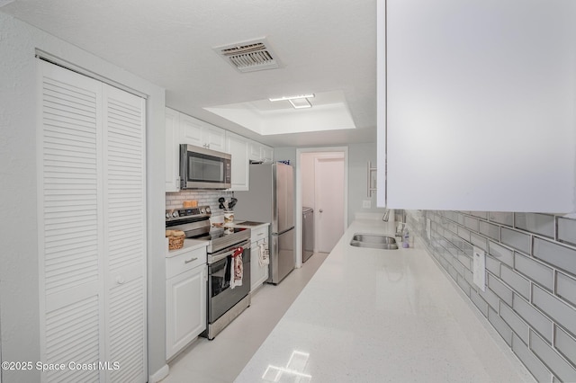 kitchen featuring tasteful backsplash, visible vents, a raised ceiling, appliances with stainless steel finishes, and a sink