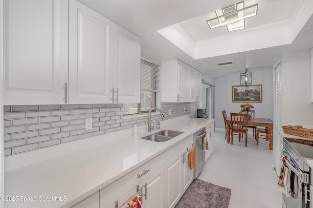 kitchen featuring tasteful backsplash, a raised ceiling, appliances with stainless steel finishes, white cabinetry, and a sink