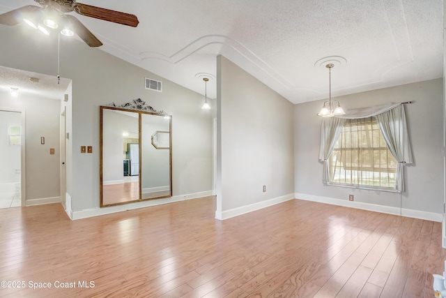 empty room featuring visible vents, light wood-style flooring, vaulted ceiling, a textured ceiling, and ceiling fan with notable chandelier