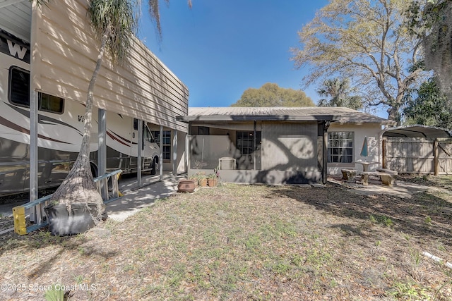 rear view of house featuring a carport, a sunroom, and fence