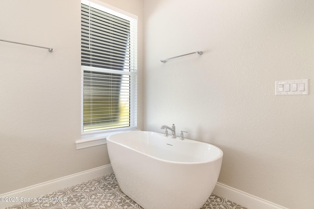 bathroom featuring baseboards, a freestanding bath, and tile patterned flooring