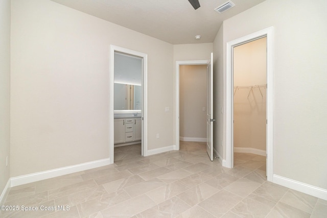 unfurnished bedroom with a walk in closet, ensuite bath, baseboards, and visible vents