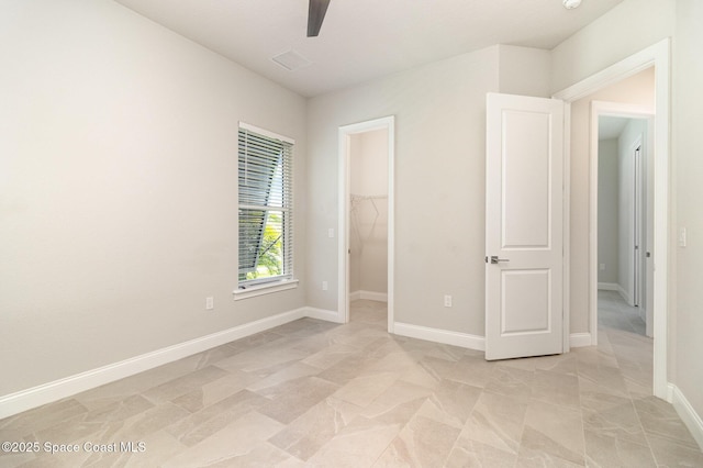 unfurnished bedroom featuring a spacious closet, ceiling fan, a closet, and baseboards