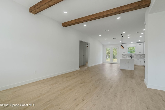 unfurnished living room with baseboards, light wood-style flooring, beam ceiling, french doors, and a sink