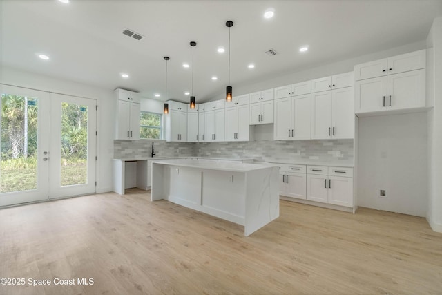 kitchen featuring light wood-type flooring, visible vents, a kitchen island, and backsplash