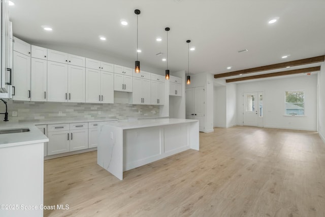 kitchen with a center island, backsplash, a sink, light wood-type flooring, and beamed ceiling