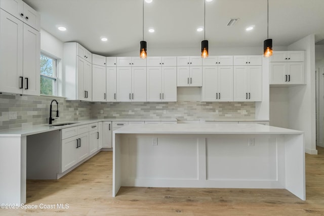 kitchen featuring light wood finished floors, lofted ceiling, a kitchen island, white cabinetry, and a sink