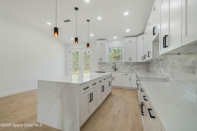 kitchen with light wood finished floors, a center island, light stone counters, and decorative backsplash