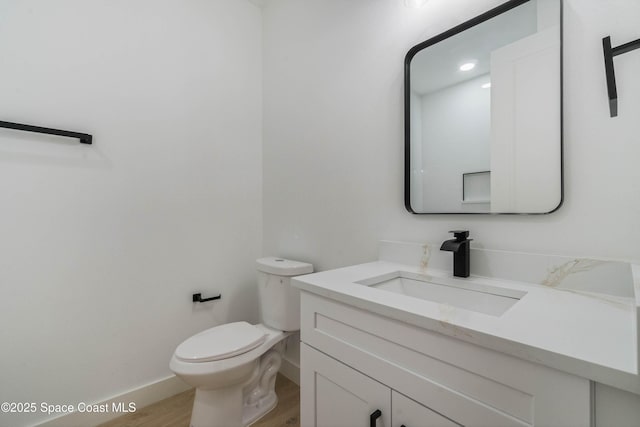 half bath featuring wood finished floors, vanity, toilet, and baseboards