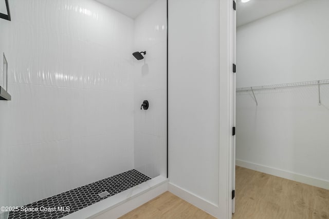 bathroom featuring a tile shower, a spacious closet, baseboards, and wood finished floors