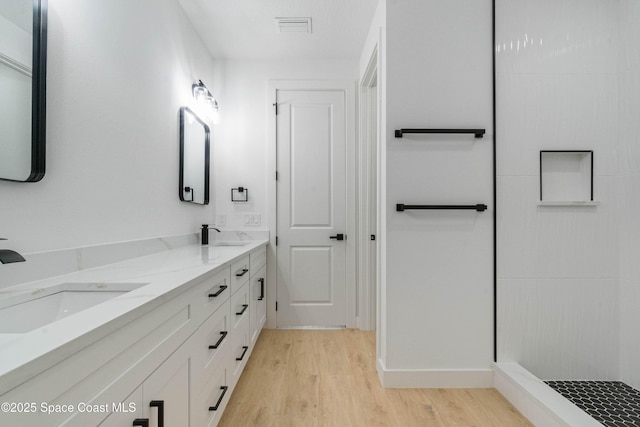 full bathroom with double vanity, visible vents, a sink, and wood finished floors