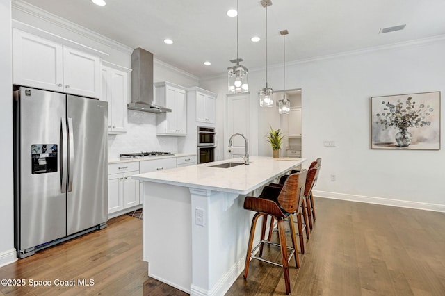 kitchen with visible vents, an island with sink, a sink, stainless steel appliances, and wall chimney exhaust hood
