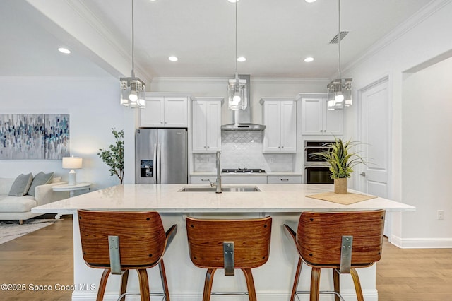 kitchen featuring visible vents, wall chimney range hood, a kitchen bar, appliances with stainless steel finishes, and light wood-style floors