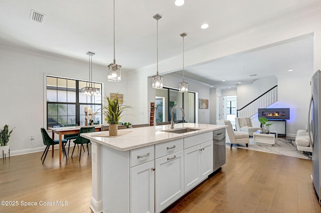 kitchen featuring crown molding, open floor plan, a center island with sink, wood finished floors, and a sink