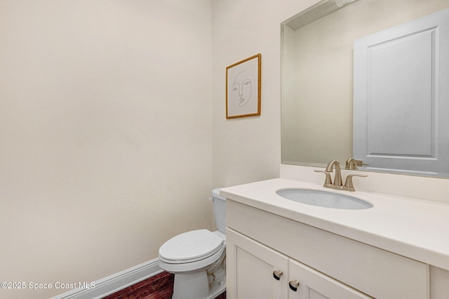 half bathroom with toilet, vanity, baseboards, and wood finished floors