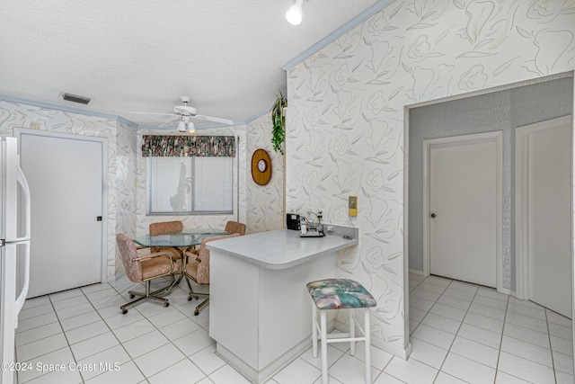 kitchen with light tile patterned floors, light countertops, a ceiling fan, a textured ceiling, and wallpapered walls