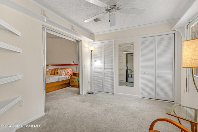 bedroom featuring a textured ceiling, ceiling fan, carpet flooring, visible vents, and two closets