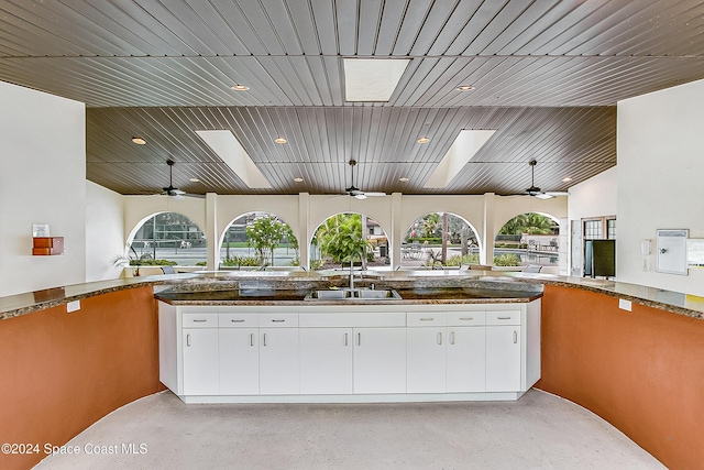 kitchen with a skylight, a sink, a ceiling fan, white cabinets, and open floor plan