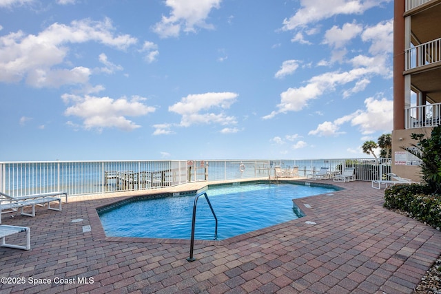 community pool with a patio area, fence, and a water view