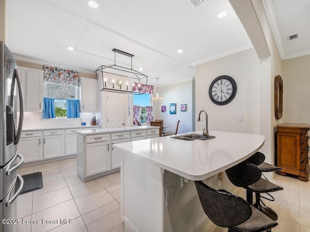 kitchen featuring white cabinets, stainless steel fridge with ice dispenser, an island with sink, ornamental molding, and a sink