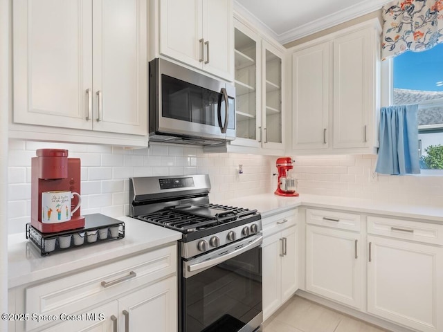 kitchen featuring tasteful backsplash, white cabinets, glass insert cabinets, appliances with stainless steel finishes, and light countertops