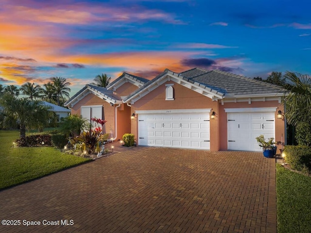 single story home with a garage, a lawn, a tiled roof, decorative driveway, and stucco siding