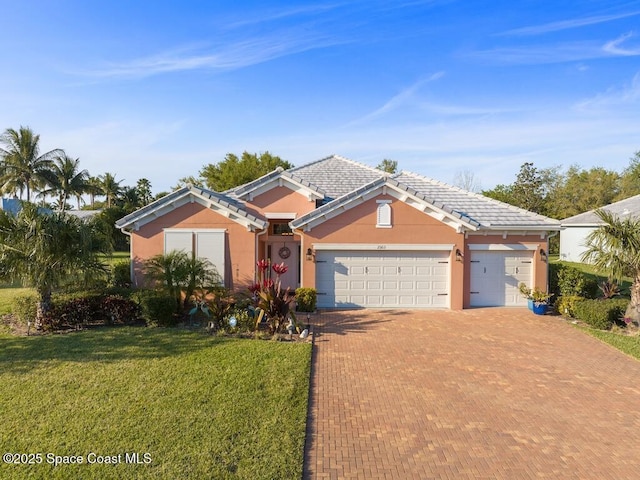 view of front of house with decorative driveway, stucco siding, an attached garage, a front yard, and a tiled roof