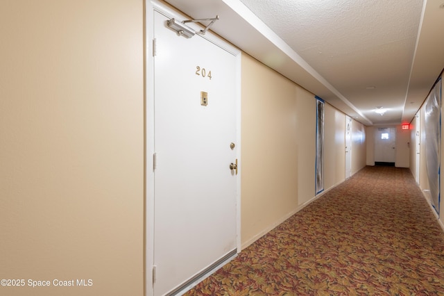 hall featuring carpet flooring, a textured ceiling, and baseboards