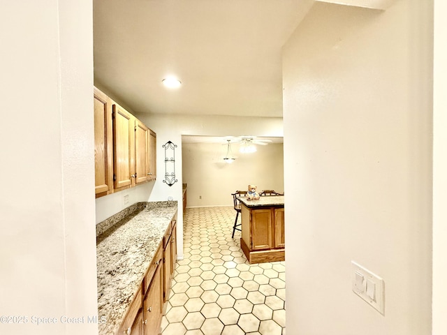 kitchen with ceiling fan, light stone counters, and brown cabinetry