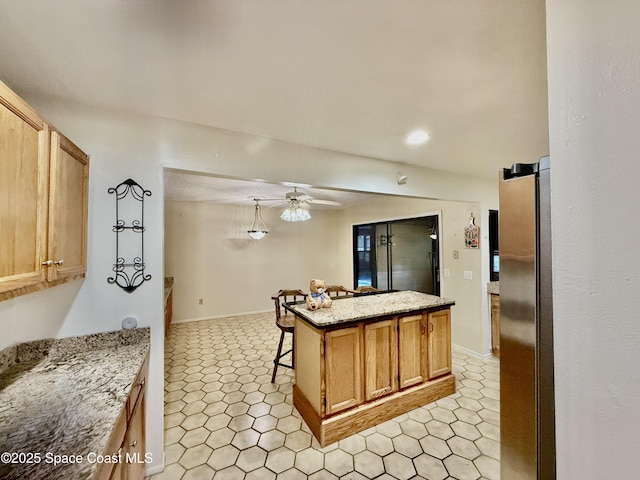 kitchen featuring a barn door, ceiling fan, a kitchen island, light stone counters, and freestanding refrigerator