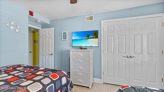 bedroom featuring a closet, visible vents, a textured ceiling, and light tile patterned floors