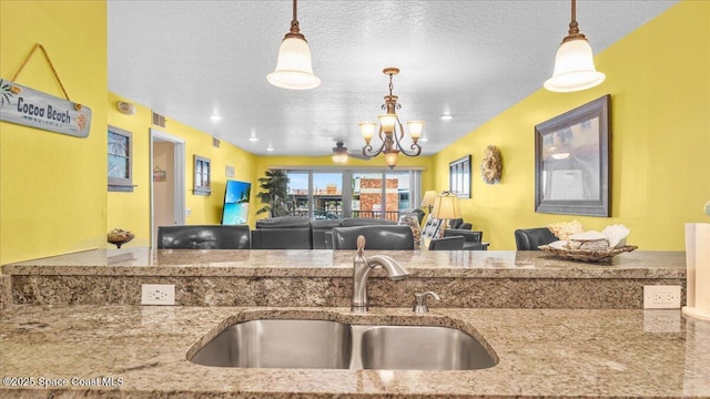 kitchen with stone countertops, open floor plan, a textured ceiling, a chandelier, and a sink